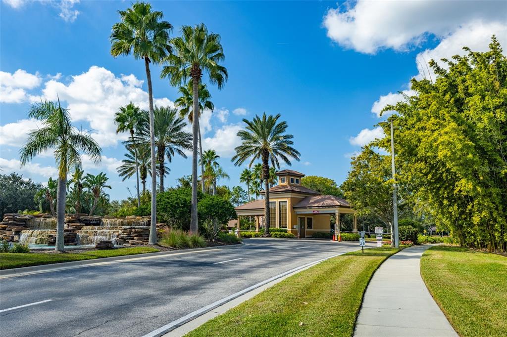 A gated community entrance features a stone waterfall, palm trees, and a guardhouse building — 5808 HIDDEN FALLS LANE, APOLLO BEACH, FL
