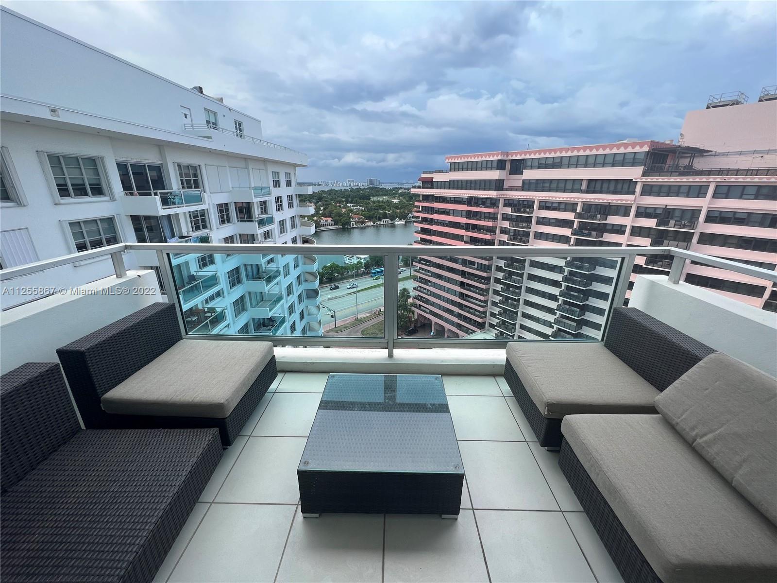 A balcony with outdoor furniture overlooks a waterway between two large apartment buildings — 5161 Collins Ave # 1711, Miami Beach FL 33140, MIAMI BEACH, FL