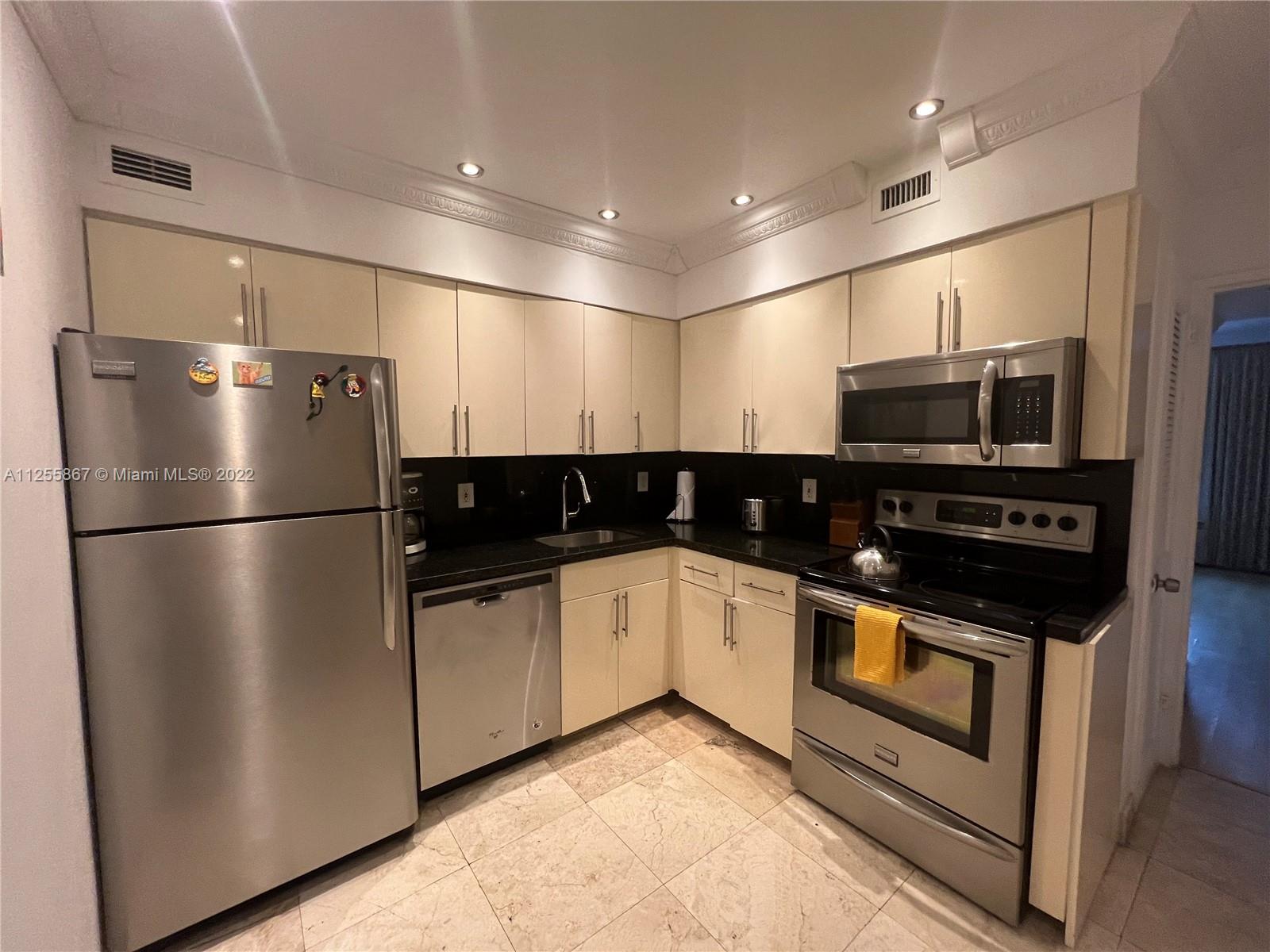 A kitchen features stainless steel appliances, cream-colored cabinets, black countertops, and light-colored tile flooring — 5161 Collins Ave # 1711, Miami Beach FL 33140, MIAMI BEACH, FL