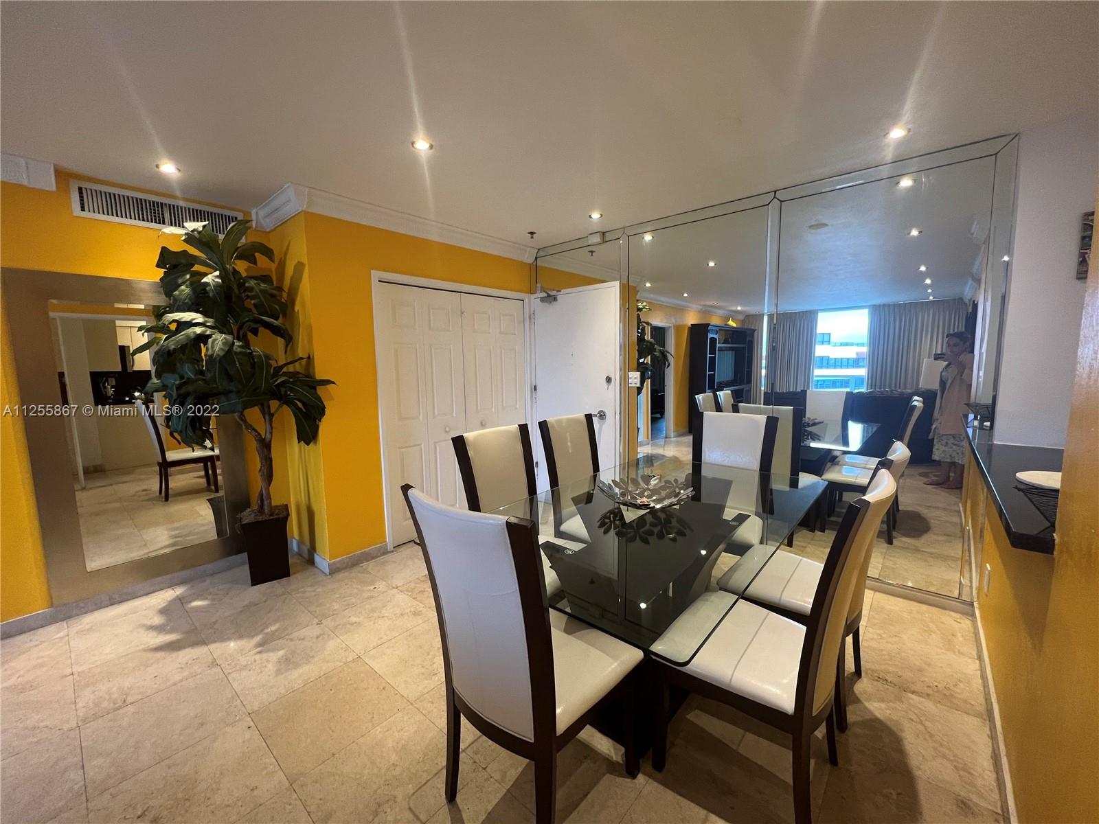 A dining room features a glass-topped table, white chairs, yellow walls, and mirrored accent walls — 5161 Collins Ave # 1711, Miami Beach FL 33140, MIAMI BEACH, FL