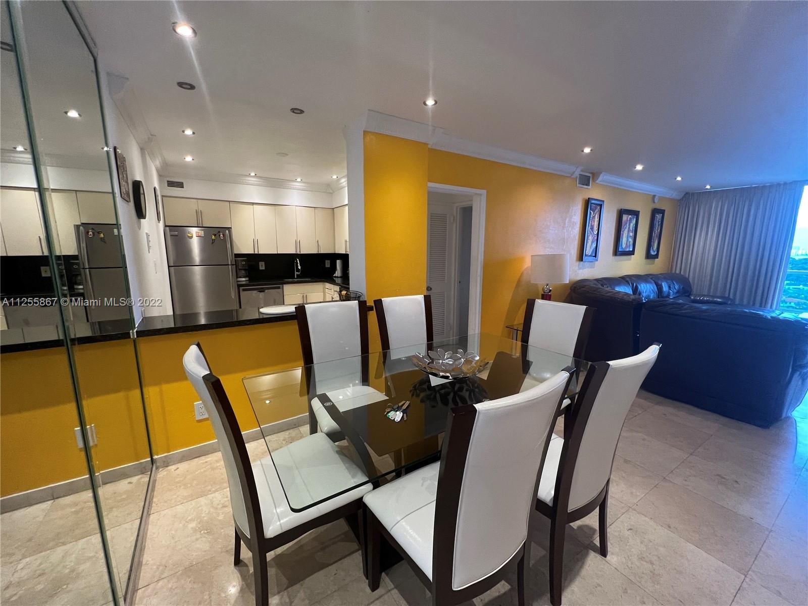 A dining area features a glass table with six white chairs against a yellow wall — 5161 Collins Ave # 1711, Miami Beach FL 33140, MIAMI BEACH, FL