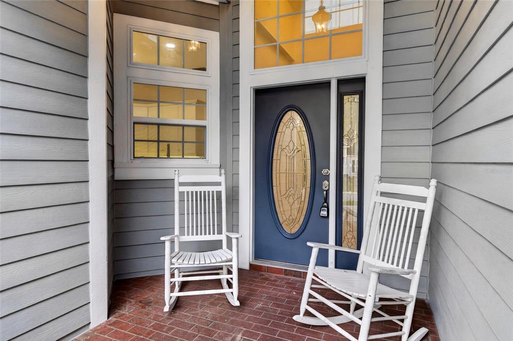 A front porch with two white rocking chairs, a blue front door, and brick flooring — 914 SW 83RD TERRACE, GAINESVILLE, FL