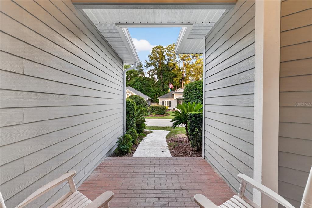 A covered brick entryway with two white chairs faces a walkway and neighborhood street — 914 SW 83RD TERRACE, GAINESVILLE, FL