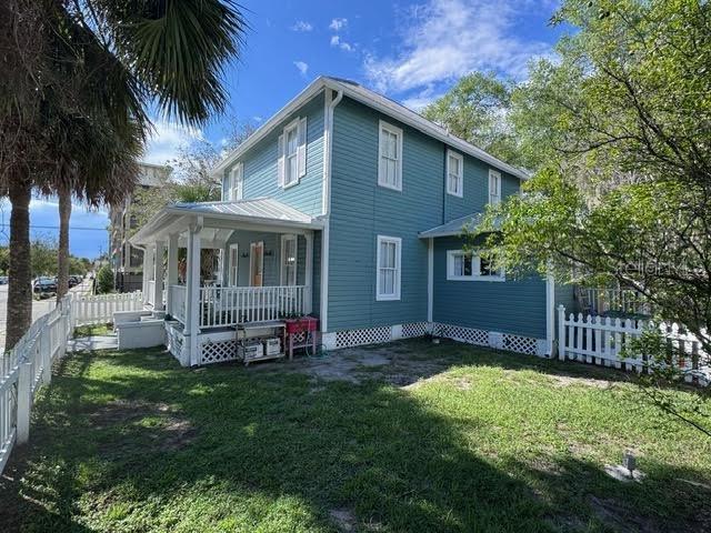 A two-story blue house with a wrap-around porch and white trim stands on a lawn — 201 E VOORHIS AVENUE, DELAND, FL