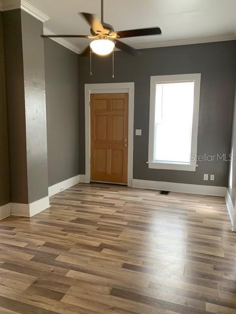 An empty room features gray walls, wood-look flooring, a ceiling fan, and a wooden door — 201 E VOORHIS AVENUE, DELAND, FL