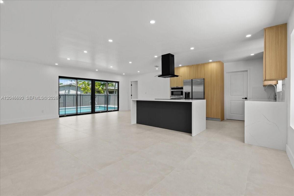 A modern kitchen with a black island, light wood cabinetry, and sliding glass doors — 15920 SW 105th Ave, Miami FL 33157, MIAMI, FL