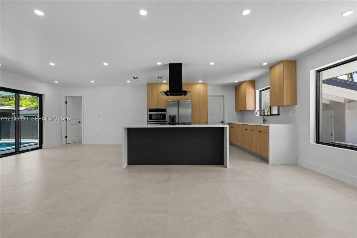 A modern kitchen features a black island, light wood cabinetry, and white tile flooring — 15920 SW 105th Ave, Miami FL 33157, MIAMI, FL