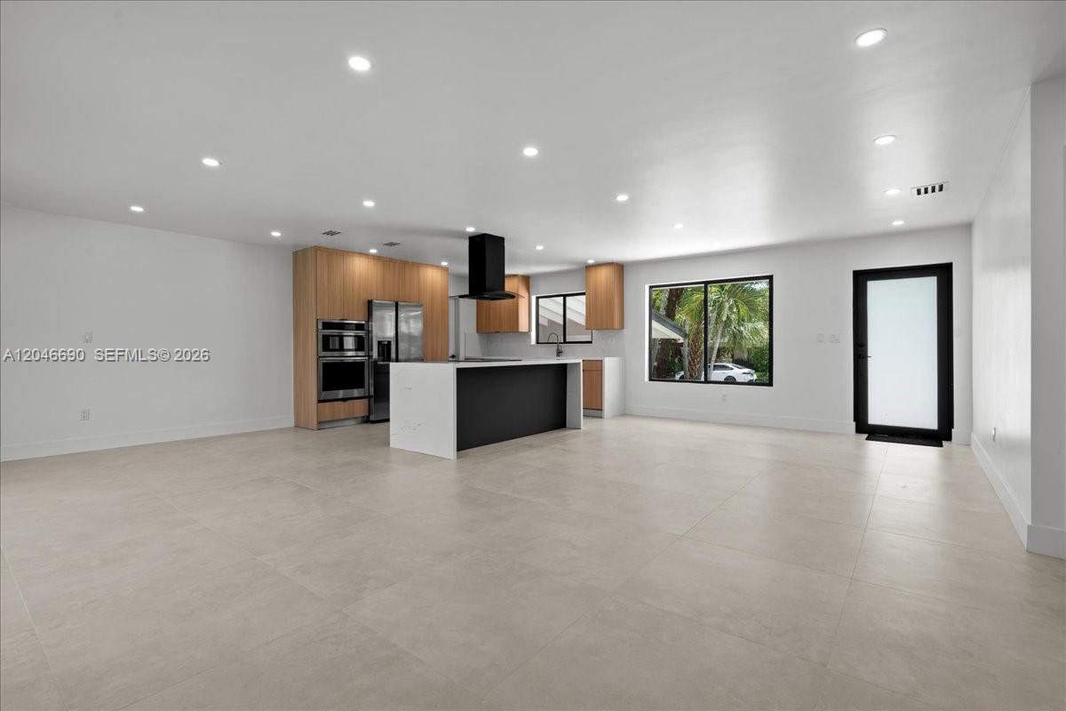 A modern kitchen features light wood cabinetry, a black island, and large light-colored floor tiles — 15920 SW 105th Ave, Miami FL 33157, MIAMI, FL