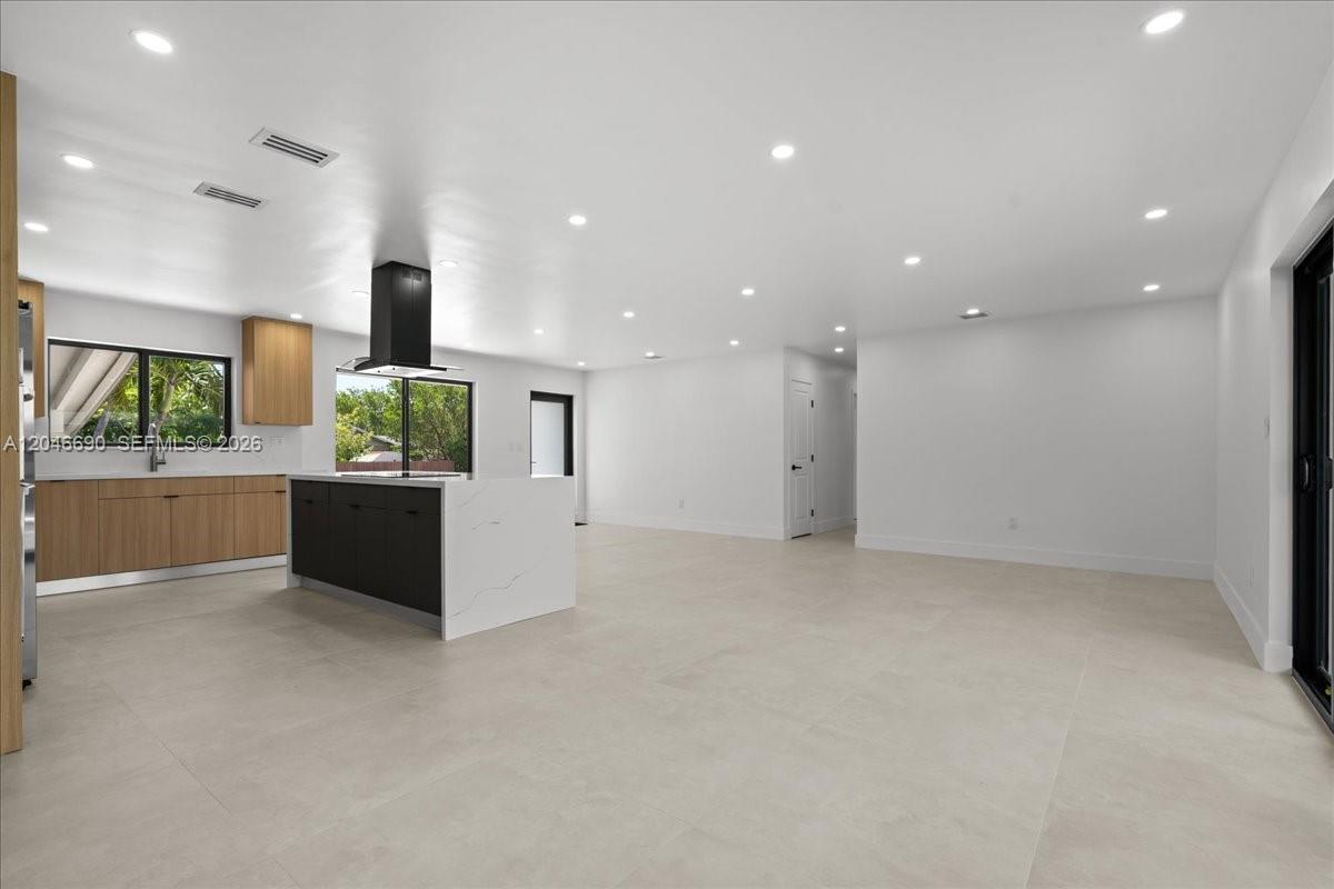 A modern kitchen features a white island, light wood cabinetry, and large floor tiles — 15920 SW 105th Ave, Miami FL 33157, MIAMI, FL