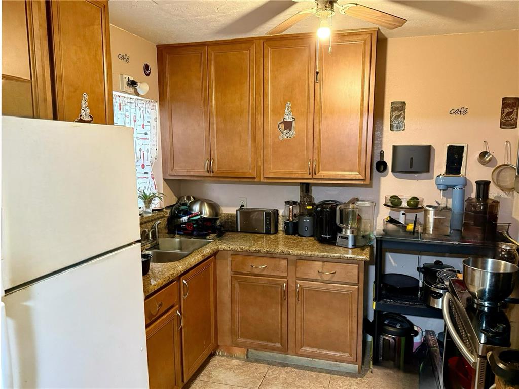 A kitchen features wood cabinets, granite countertops, a stainless steel sink, and various small appliances — 6233 BALBOA DRIVE, ORLANDO, FL
