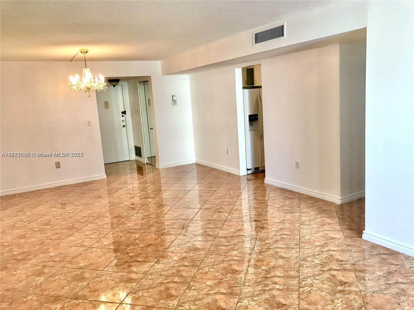 An empty room features glossy brown marble-patterned tile flooring and a crystal chandelier — 1833 S Ocean Dr # 305, Hallandale Beach FL 33009, HALLANDALE BEACH, FL