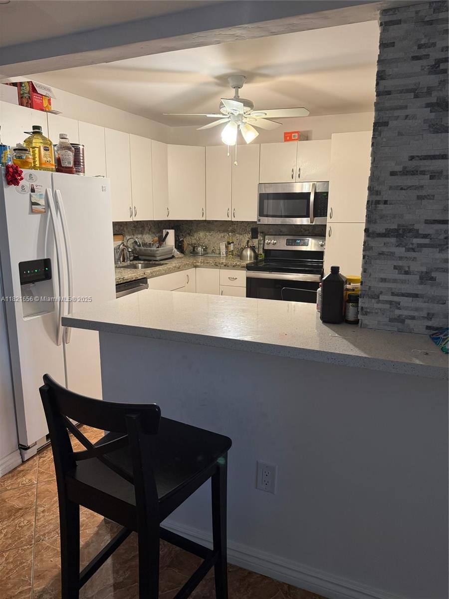 A kitchen features white cabinets, a breakfast bar, and a stone-tiled accent wall — 1833 S Ocean Dr # 305, Hallandale Beach FL 33009, HALLANDALE BEACH, FL