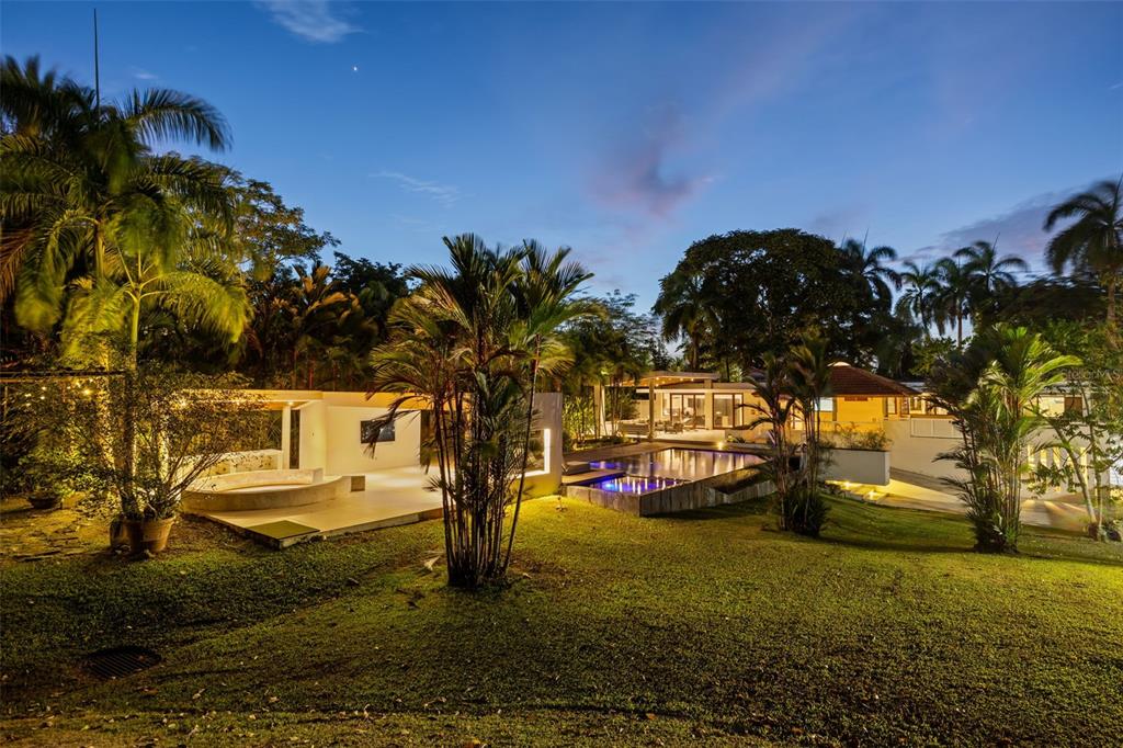 A backyard at twilight features a modern house, a swimming pool, and lush palm trees — 1841 BEGONIA ST, SANTA MARIA, SAN JUAN, PR
