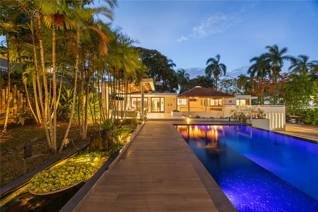 A wooden walkway leads toward a modern house with a pool and lush tropical landscaping — 1841 BEGONIA ST, SANTA MARIA, SAN JUAN, PR