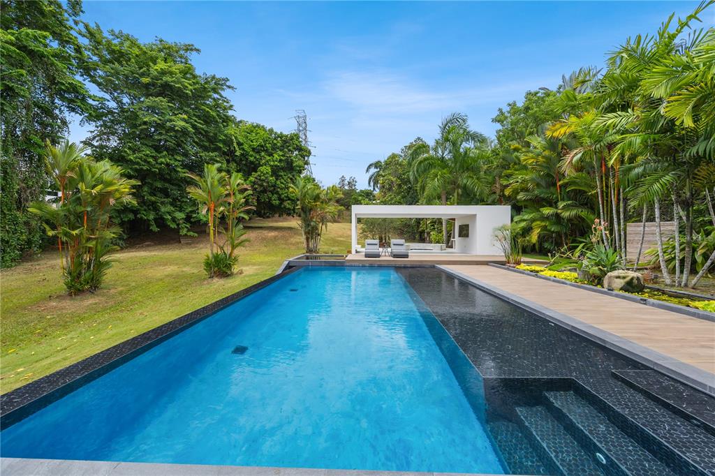 A rectangular infinity pool with dark tile steps sits beside a modern white outdoor pavilion — 1841 BEGONIA ST, SANTA MARIA, SAN JUAN, PR