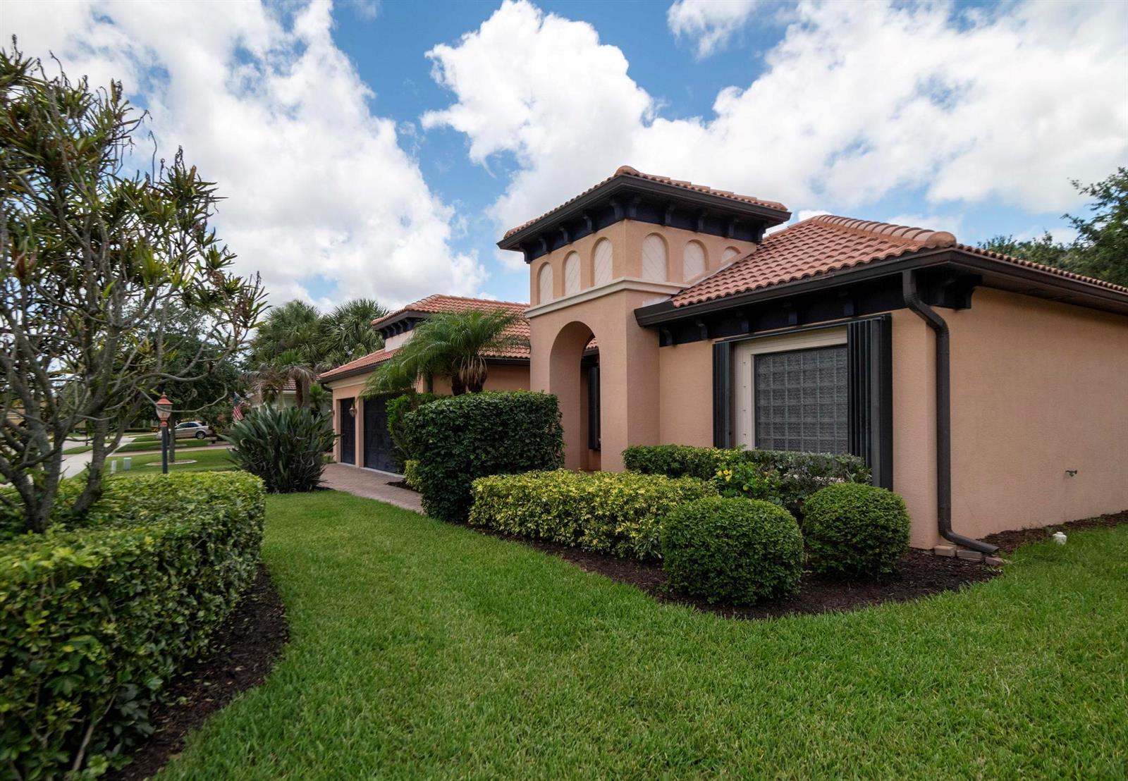 A single-story stucco house with a tile roof and manicured landscaping under a cloudy sky — 2295 NW Diamond Creek Way, Jensen Beach FL 34957, JENSEN BEACH, FL