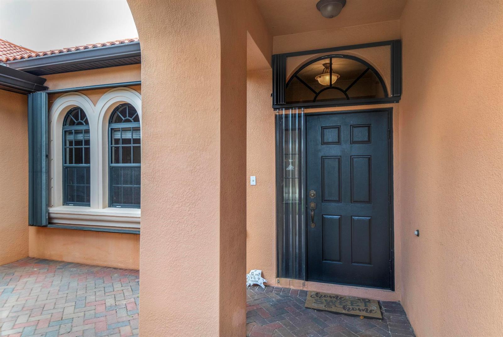 A black front door with a transom window sits under a covered entryway with stucco walls — 2295 NW Diamond Creek Way, Jensen Beach FL 34957, JENSEN BEACH, FL