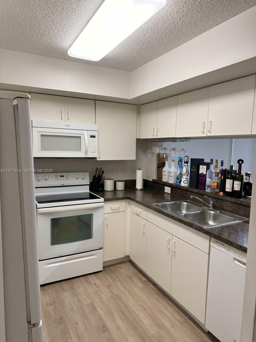 A kitchen features white cabinets, dark countertops, white appliances, and a pass-through window — 440 S Park Rd # 102, Hollywood FL 33021, HOLLYWOOD, FL