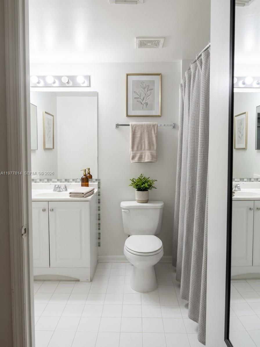 A bathroom features a white vanity, a toilet, and a shower with a gray curtain — 440 S Park Rd # 102, Hollywood FL 33021, HOLLYWOOD, FL