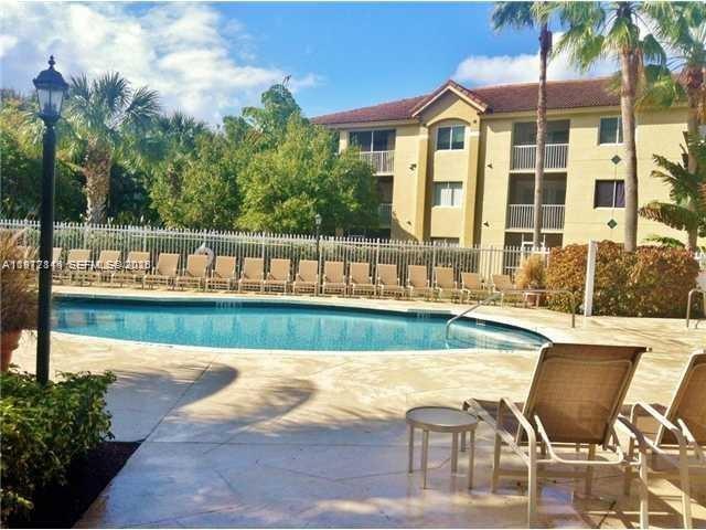 A swimming pool with lounge chairs sits in front of a multi-story apartment building — 440 S Park Rd # 102, Hollywood FL 33021, HOLLYWOOD, FL