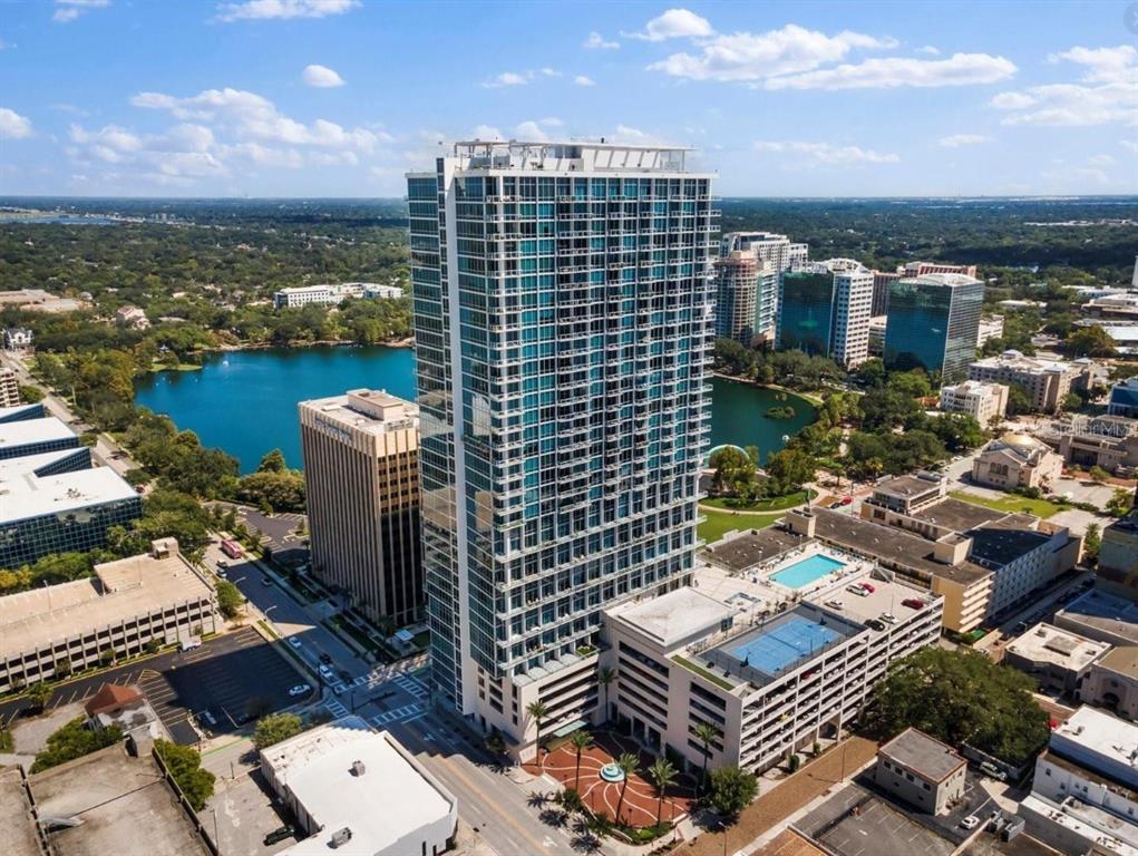 An aerial view of a tall glass residential skyscraper situated next to a lake — 150 E ROBINSON STREET UNIT 29B, ORLANDO, FL