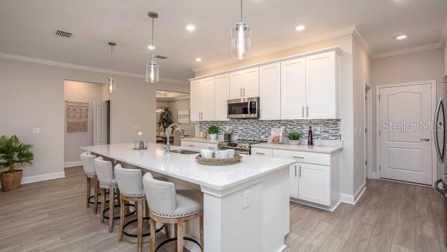 A modern kitchen features white cabinets, a large island with bar stools, and stainless appliances — 65 BELLS OF IRELAND COURT, HOMOSASSA, FL