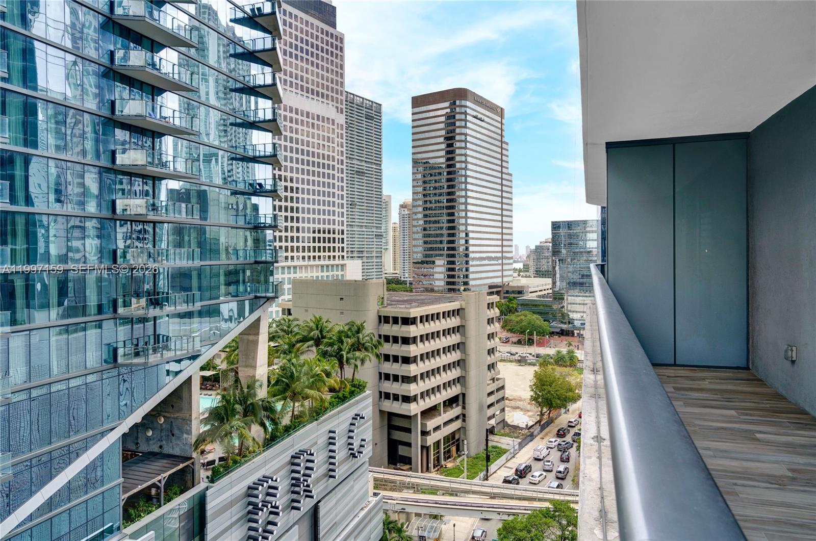 A balcony overlooks a dense urban cityscape with modern skyscrapers and a parking garage — 801 S Miami Ave # 1106, Miami FL 33130, MIAMI, FL