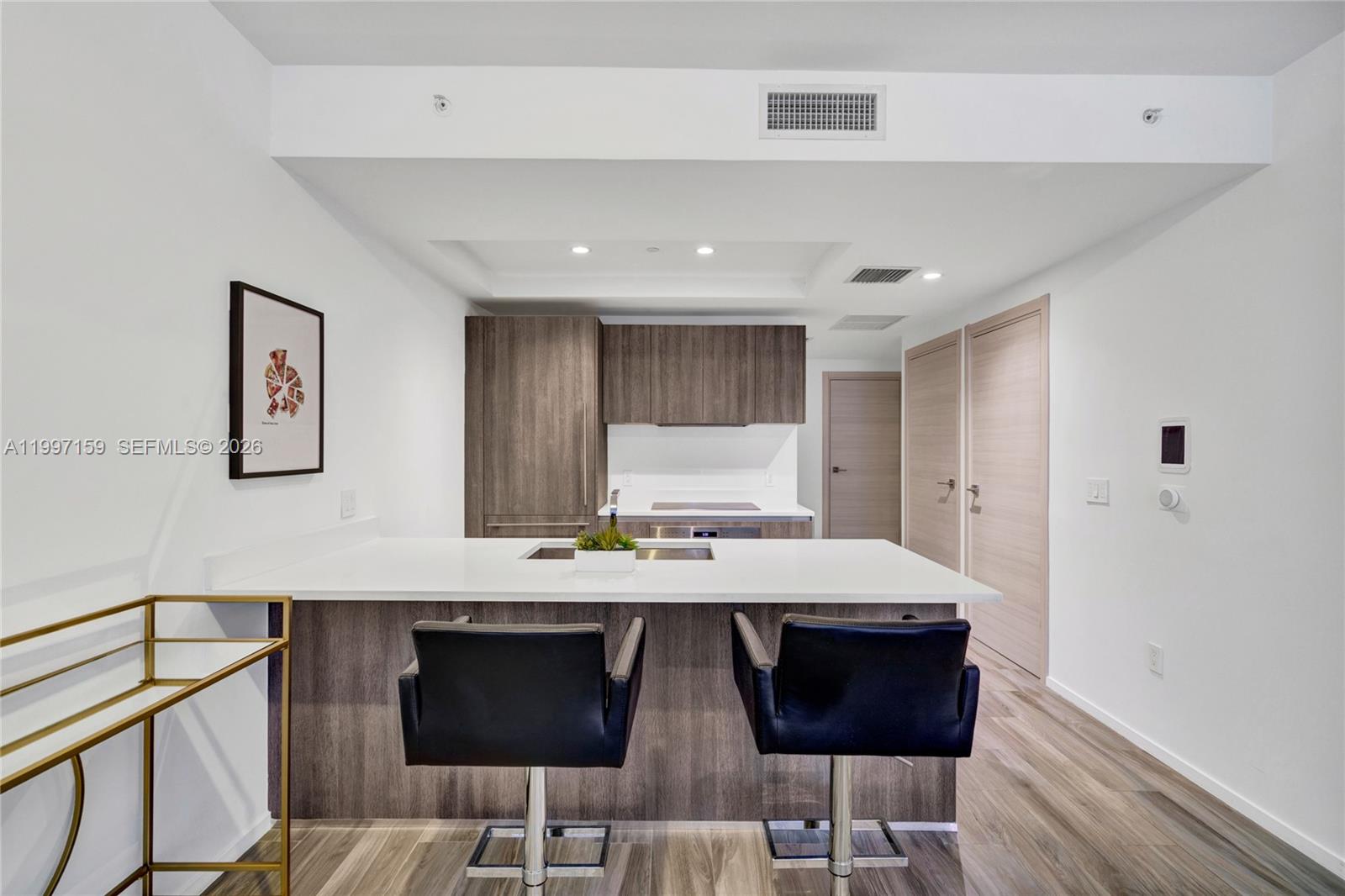 A modern kitchen features a white island, dark wood cabinetry, and two black bar stools — 801 S Miami Ave # 1106, Miami FL 33130, MIAMI, FL