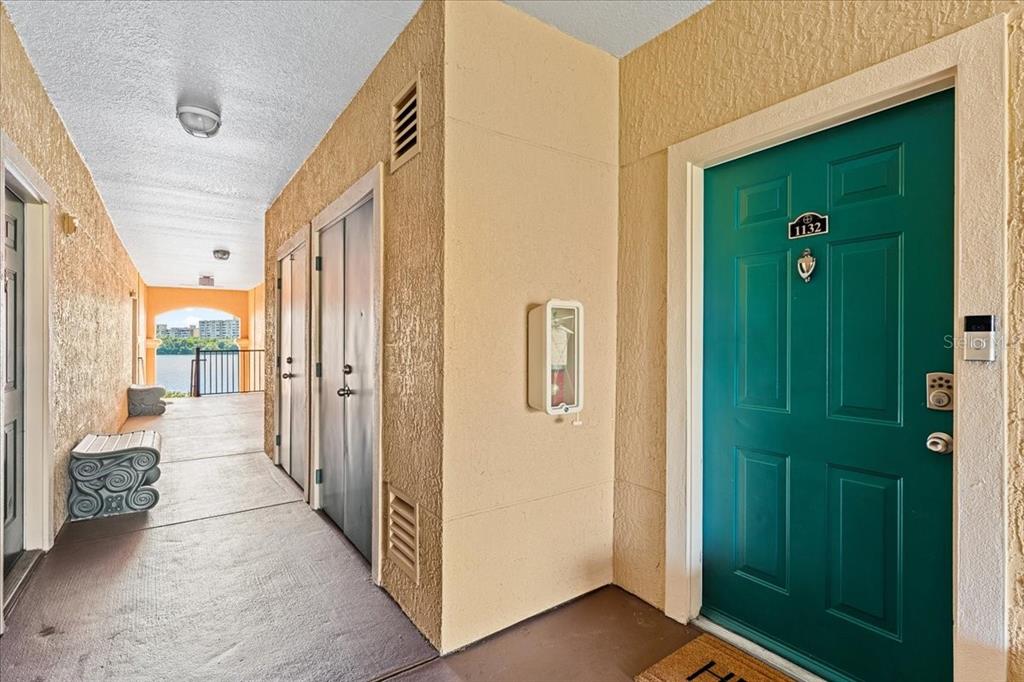 An outdoor apartment hallway features a teal front door, storage closets, and a water view — 2747 VIA CAPRI UNIT 1132, CLEARWATER, FL