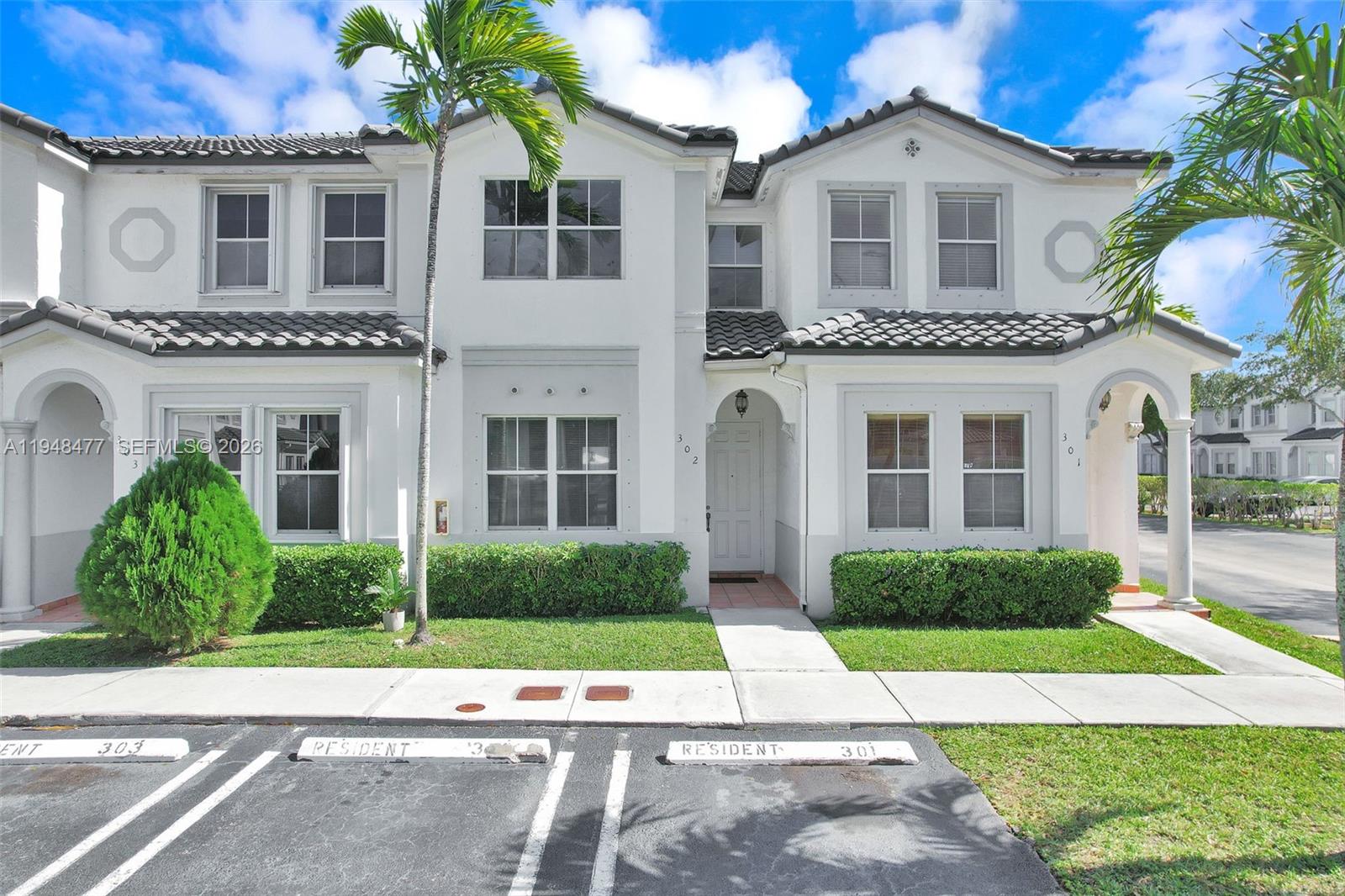 A two-story townhouse exterior features white stucco walls, a tiled roof, and dedicated parking spaces — 5420 NW 107 AVE # 302, Doral FL 33178, DORAL, FL