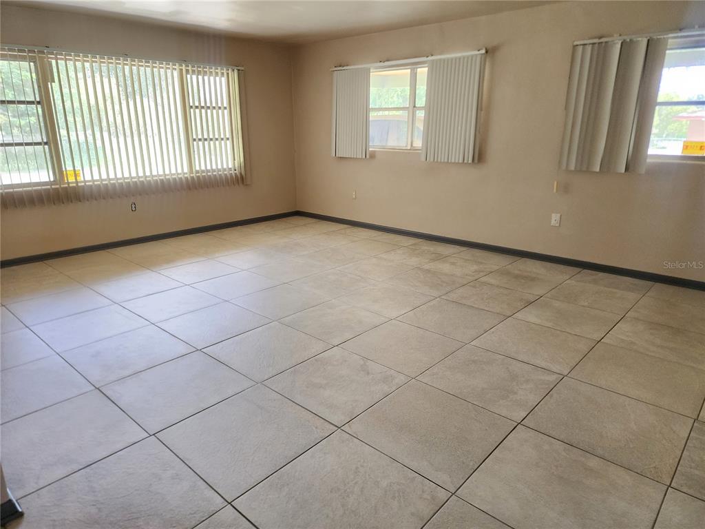 A spacious room with light-colored floor tiles, beige walls, and several windows with vertical blinds — 1104 W 14TH STREET, LAKELAND, FL