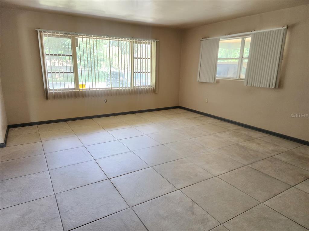 An empty room features large windows with vertical blinds and light-colored square floor tiles — 1104 W 14TH STREET, LAKELAND, FL