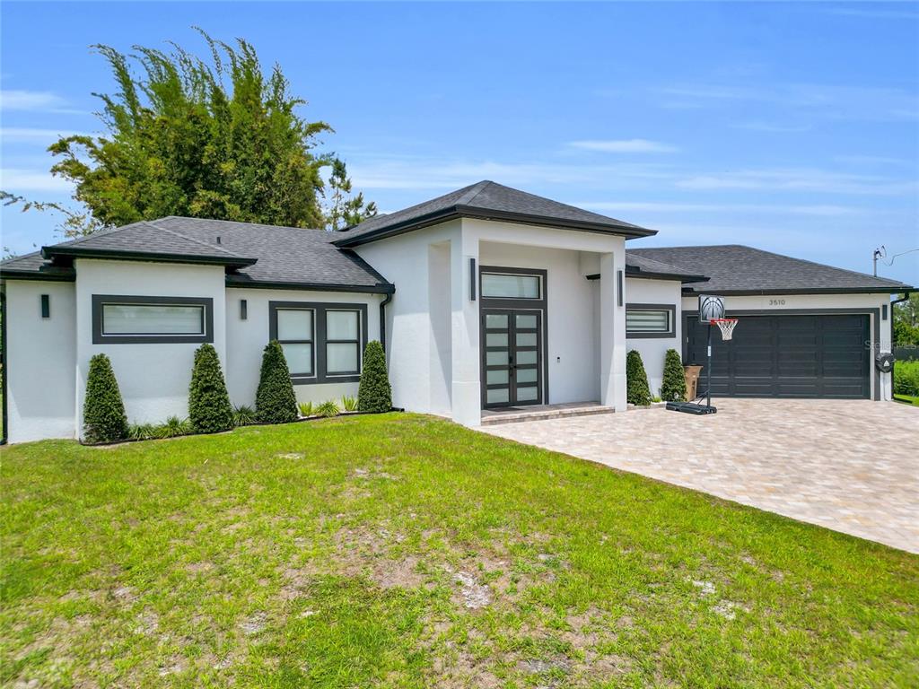 A modern single-story house with white stucco walls, dark trim, and a paved driveway — 3510 9TH COURT W, LEHIGH ACRES, FL