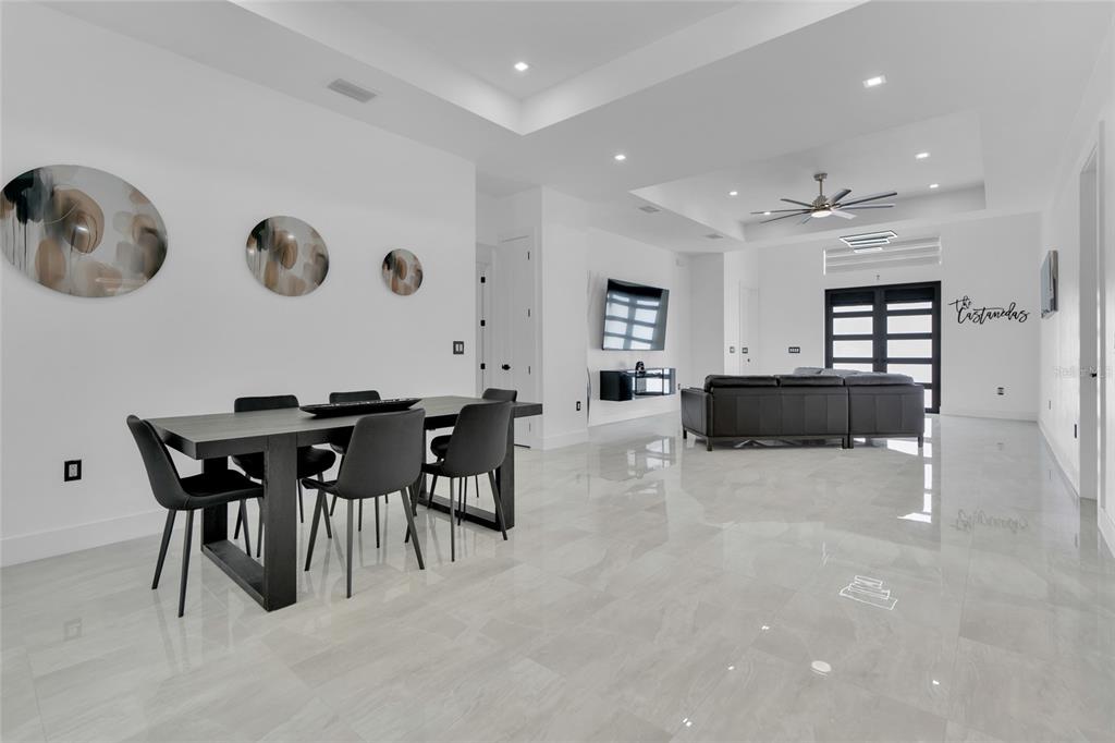 A modern open-concept living and dining area features white walls, tile flooring, and dark furniture — 3510 9TH COURT W, LEHIGH ACRES, FL