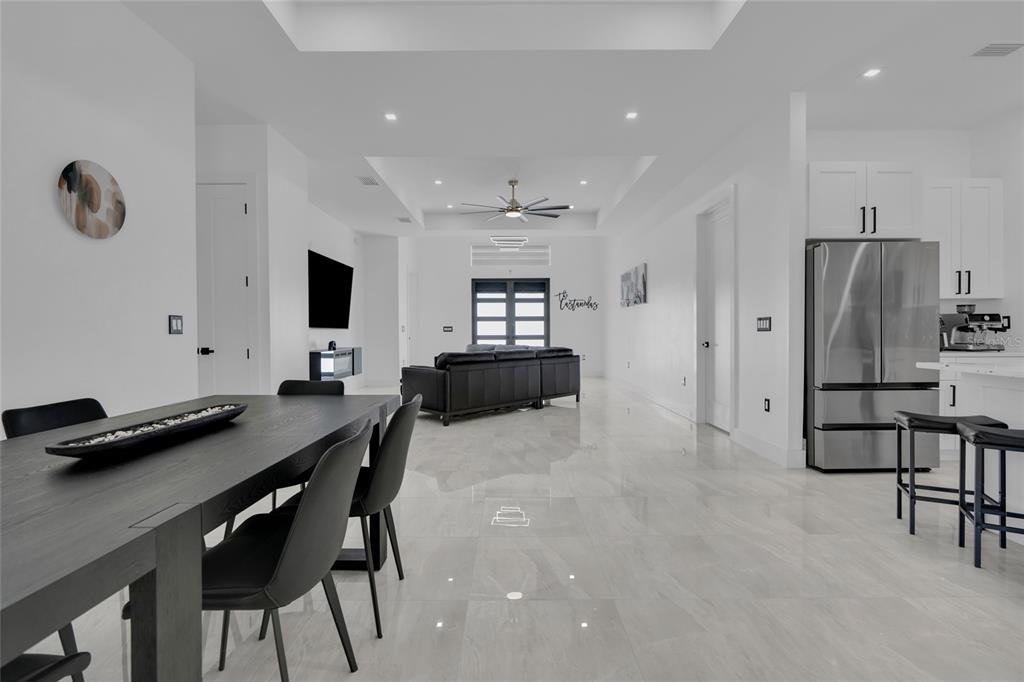 A modern open-concept living and dining area features white walls, tile floors, and dark furniture — 3510 9TH COURT W, LEHIGH ACRES, FL