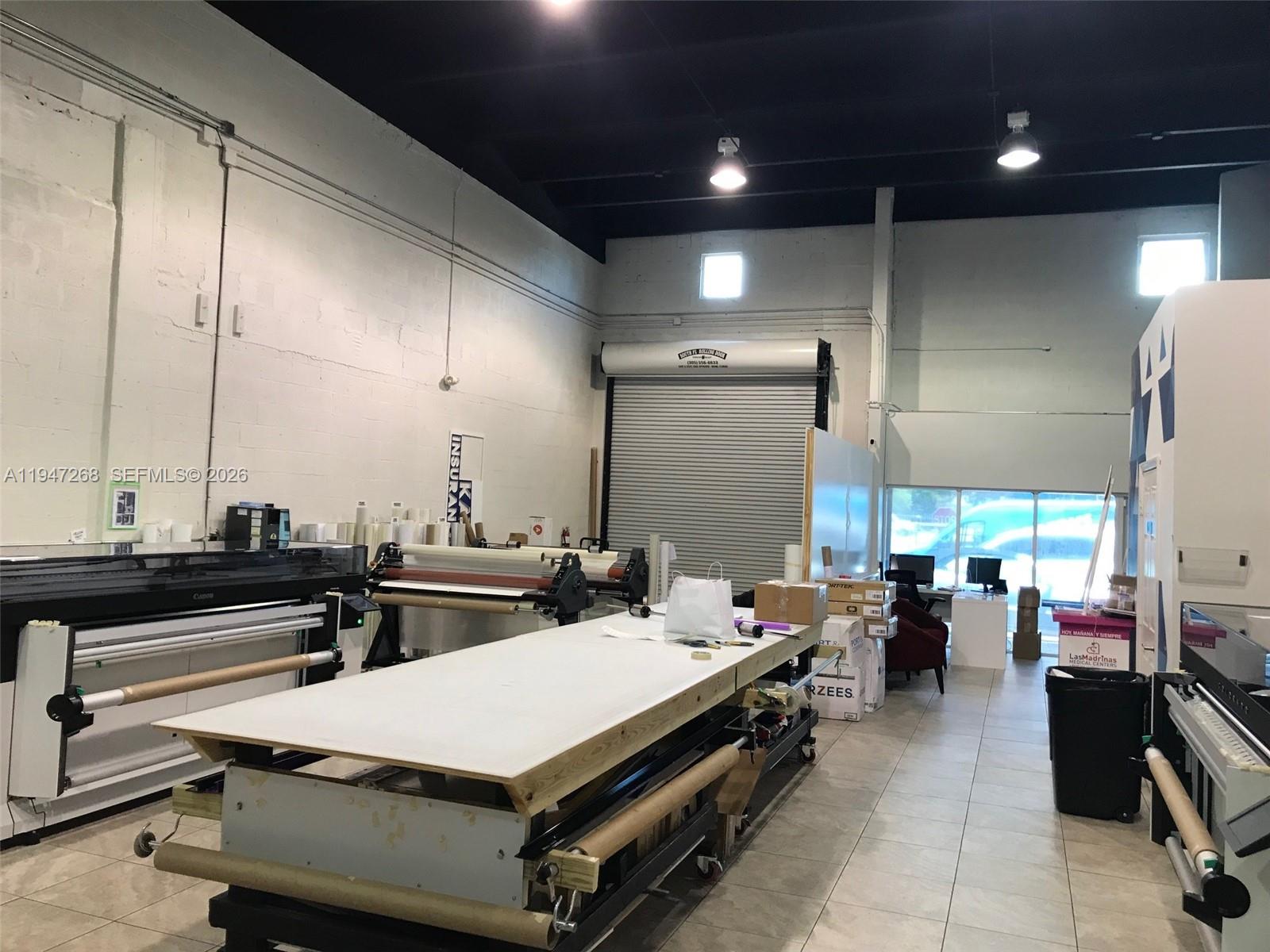 An industrial workspace features a large central work table, printing equipment, and a roll-up door — 12300 SW 130th St # 7, Miami FL 33186, MIAMI, FL