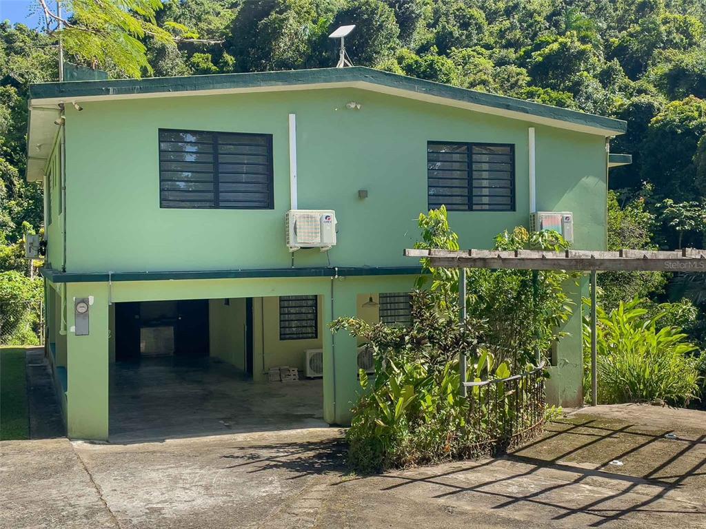 A two-story green house with a carport and a wooden pergola in a tropical setting — 38 COLINAS DE CUBUY, CANOVANAS, PR