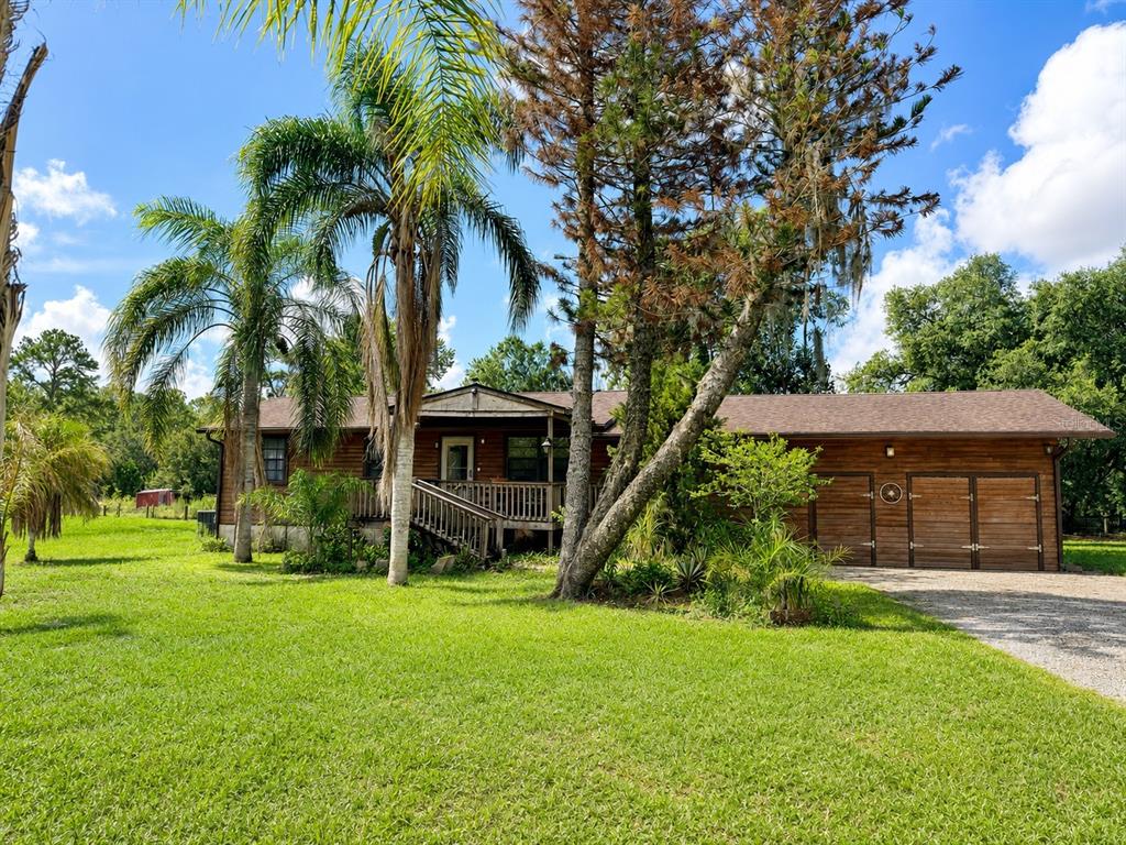 A single-story wooden house with a front porch, attached garage, and palm trees in the yard — 5280 HAYWOOD RUFFIN ROAD, ST CLOUD, FL