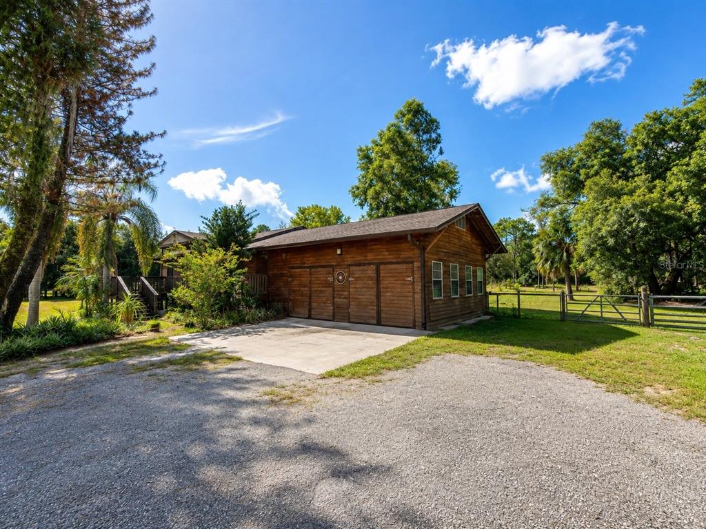 A wooden garage with a concrete driveway sits on a grassy lot with mature trees — 5280 HAYWOOD RUFFIN ROAD, ST CLOUD, FL