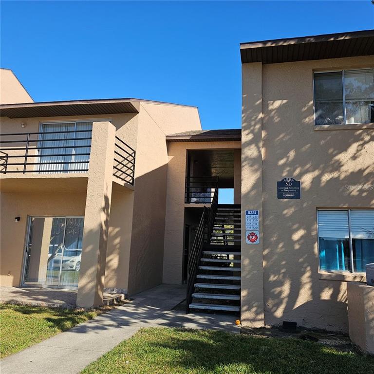 A two-story apartment building exterior features tan stucco walls, a central staircase, and sliding doors — 5231 VIA HACIENDA CIRCLE UNIT 117, ORLANDO, FL