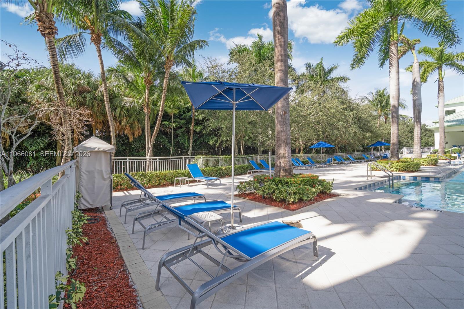 A swimming pool area features lounge chairs with blue umbrellas on a paved deck — 5300 NW 87th Ave # 108, Doral FL 33178, DORAL, FL