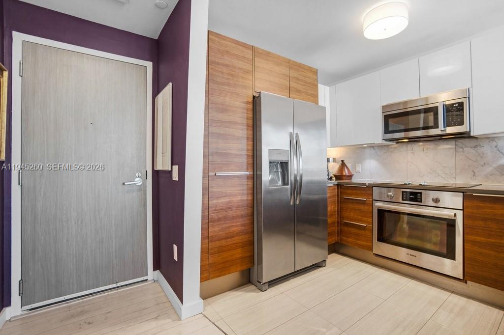 A modern kitchen features wood-grain cabinetry, stainless steel appliances, white upper cabinets, and tile flooring — 601 NE 27th St # 1505, Miami FL 33137, MIAMI, FL