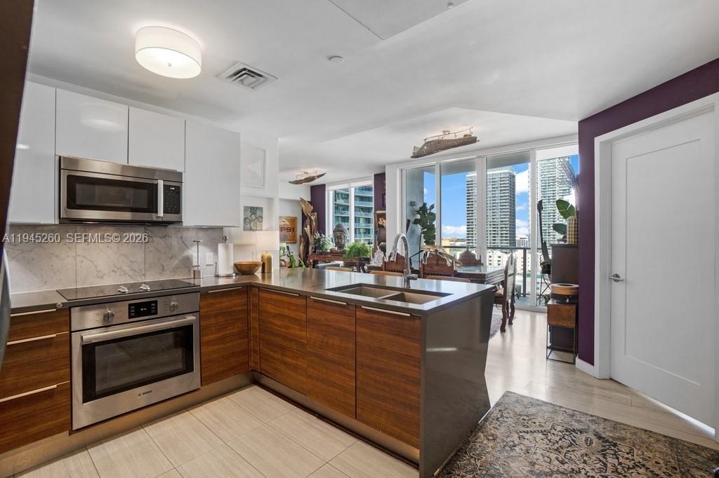 A modern kitchen features wood-grain cabinetry, stainless steel appliances, and a view of city skyscrapers — 601 NE 27th St # 1505, Miami FL 33137, MIAMI, FL