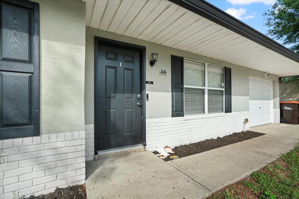 A single-story home exterior features a dark front door, white brick base, and shutters — 24 SAPPHIRE WAY, OCALA, FL