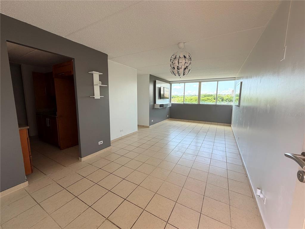 An empty living area features light tile flooring, gray accent walls, and a large window — #850 CALLE EIDER UNIT A808, SAN JUAN, PR