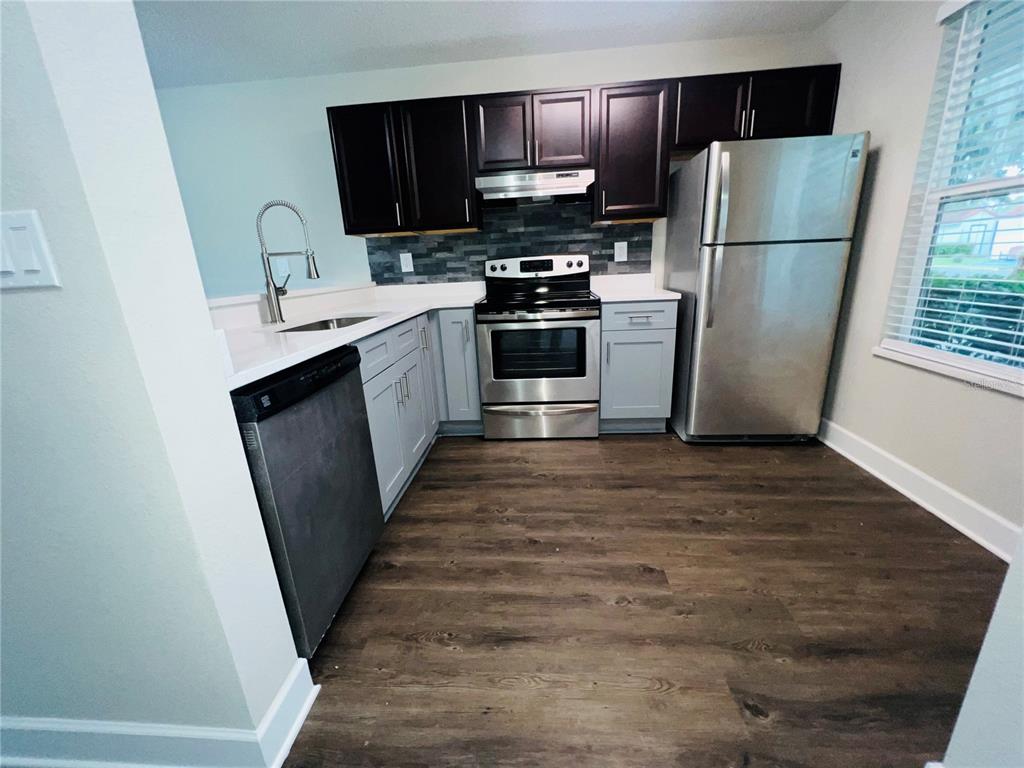 A kitchen features dark upper cabinets, light lower cabinets, stainless steel appliances, and wood flooring — 2556 WOODGATE BOULEVARD UNIT 103, ORLANDO, FL