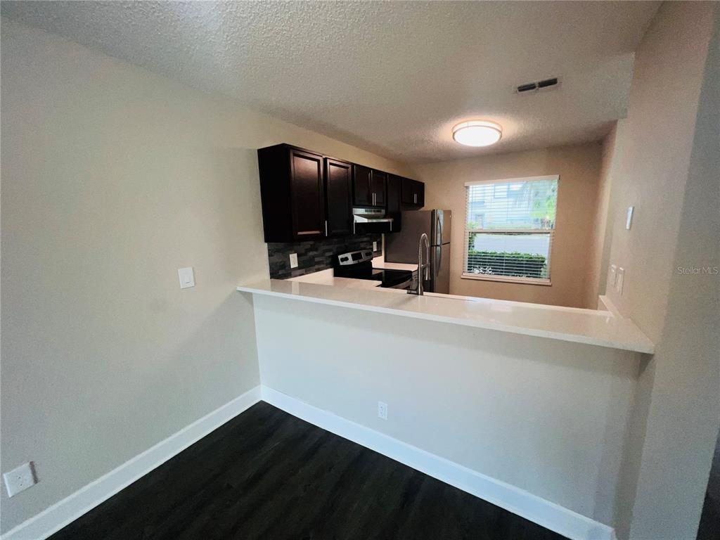 A kitchen with dark cabinets, white countertops, and a breakfast bar overlooking a window — 2556 WOODGATE BOULEVARD UNIT 103, ORLANDO, FL