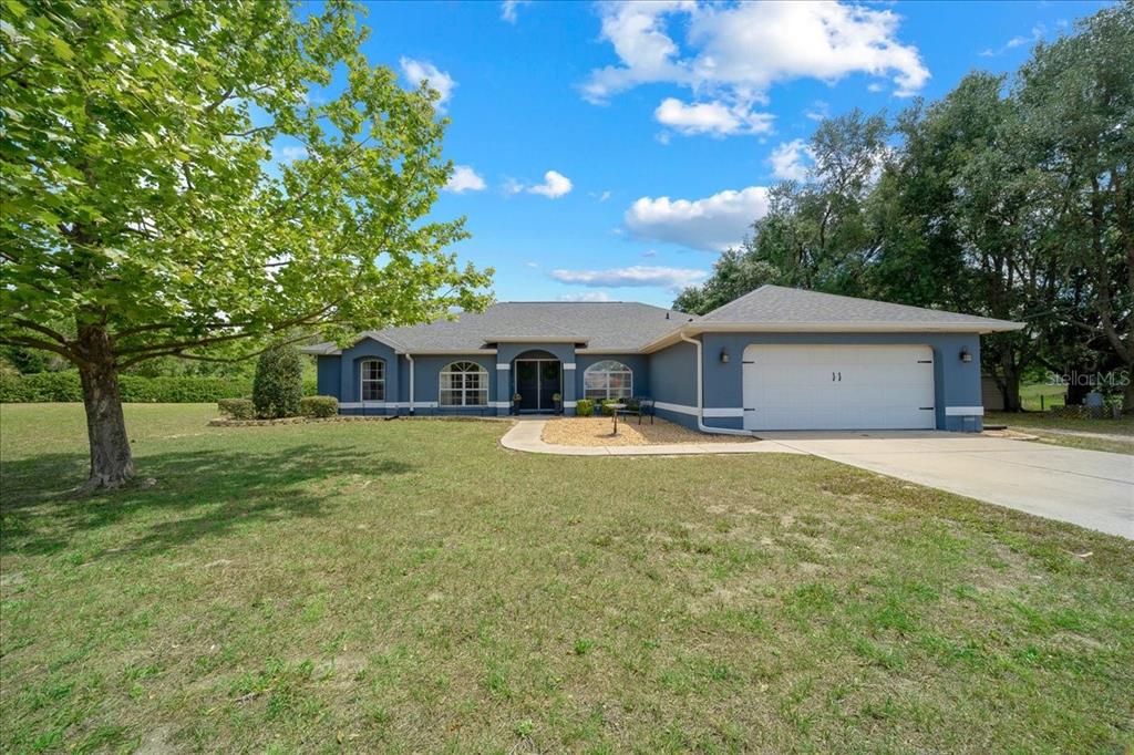 A blue single-story house with a white garage door and a large front yard — 11985 SE 123RD AVENUE, OCKLAWAHA, FL