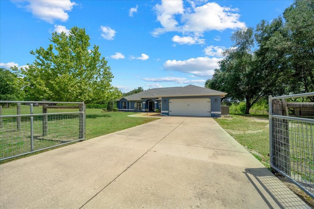 A single-story house with a two-car garage sits behind an open metal gate — 11985 SE 123RD AVENUE, OCKLAWAHA, FL