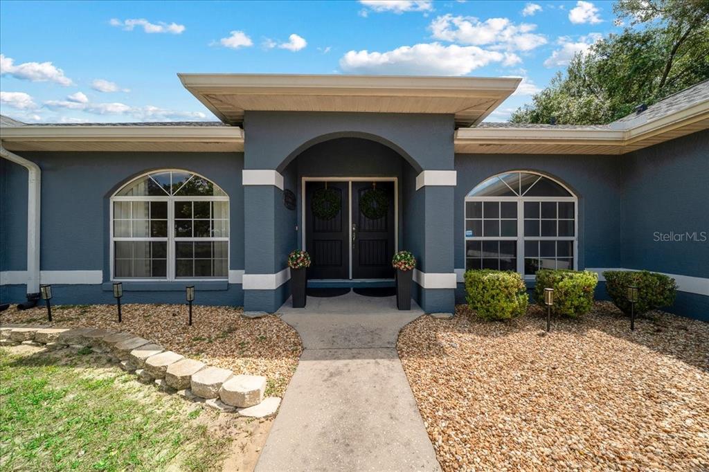 A blue house exterior features a central arched entryway with double doors and two windows — 11985 SE 123RD AVENUE, OCKLAWAHA, FL